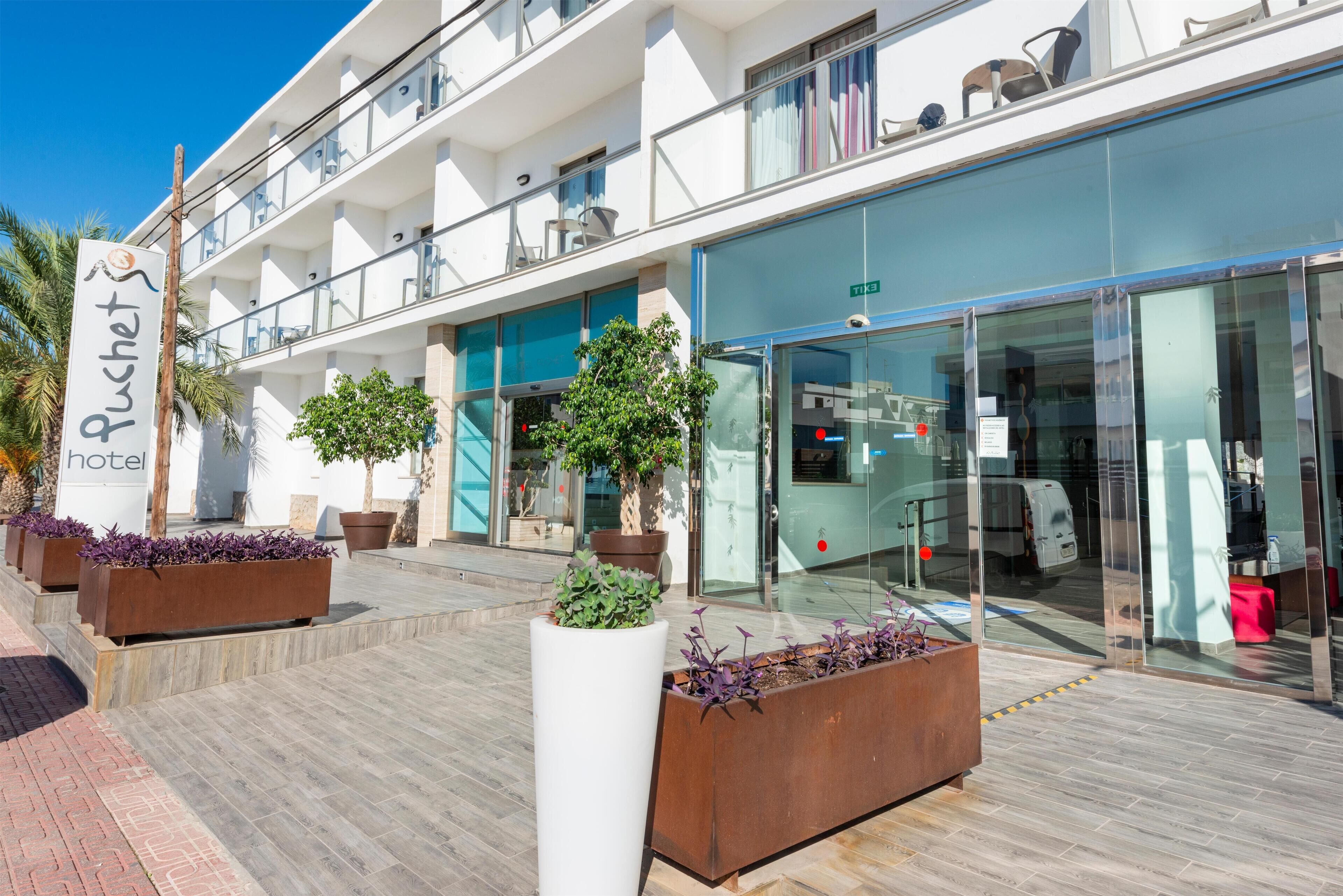 Een hotel met een modern design, met een naambord, meerdere balkons en potplanten.