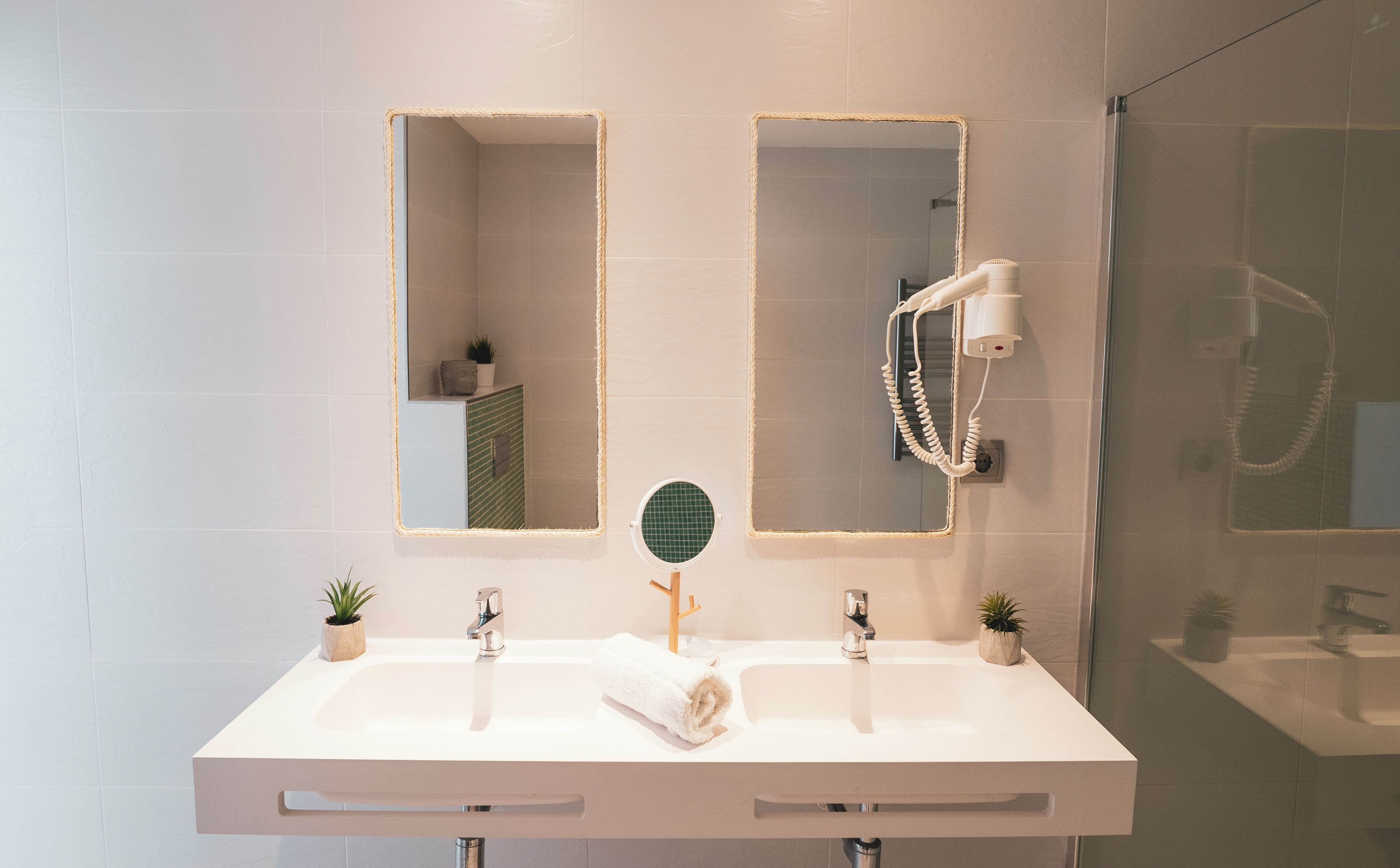 A modern bathroom with a white vanity, two mirrors, a towel, and a handheld showerhead.