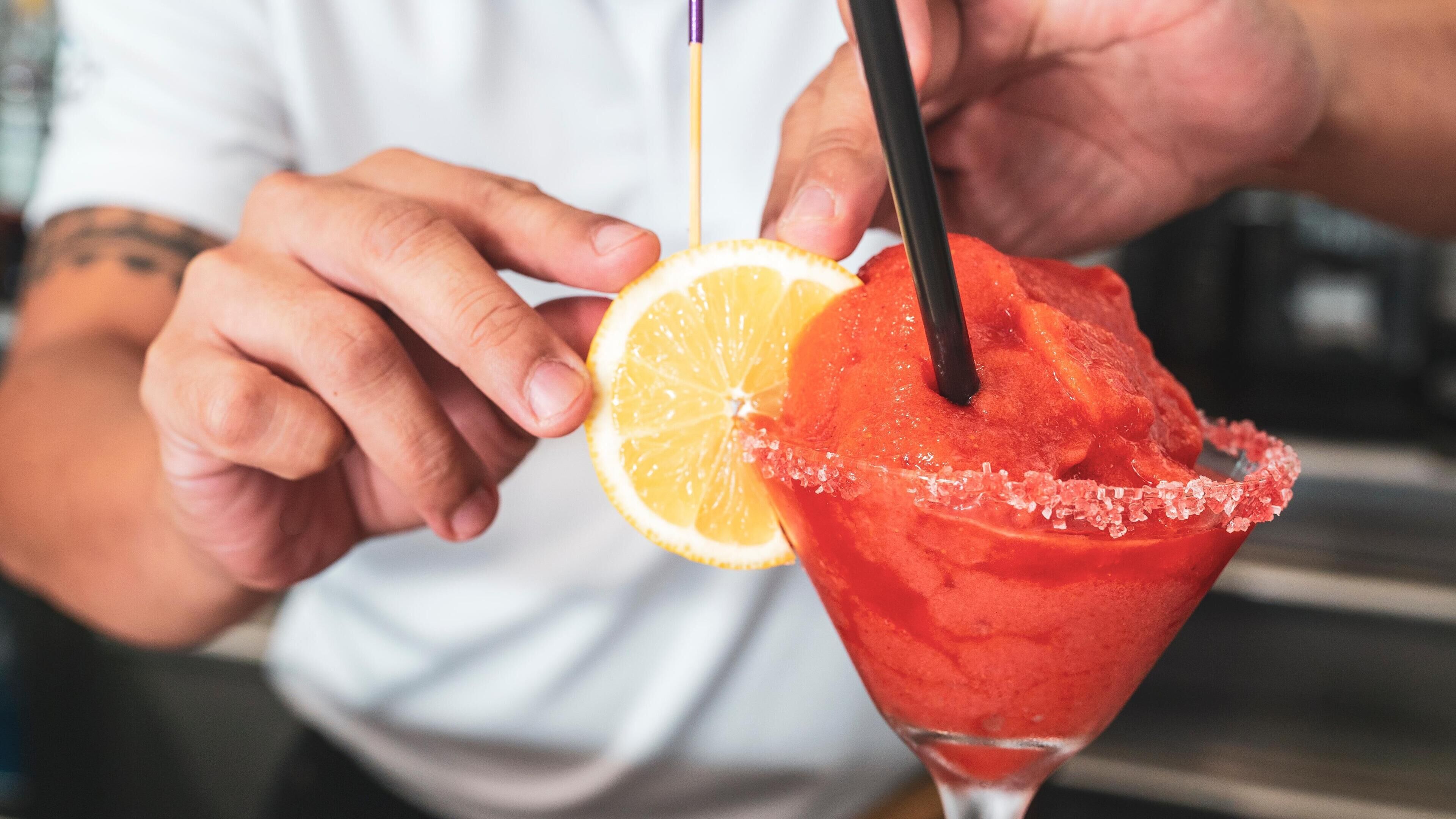 A person holding a cocktail with a salted rim and a slice of orange.