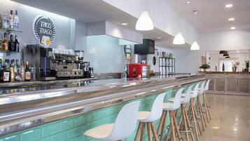Een bar met een toonbank, krukken en een koffiemachine.