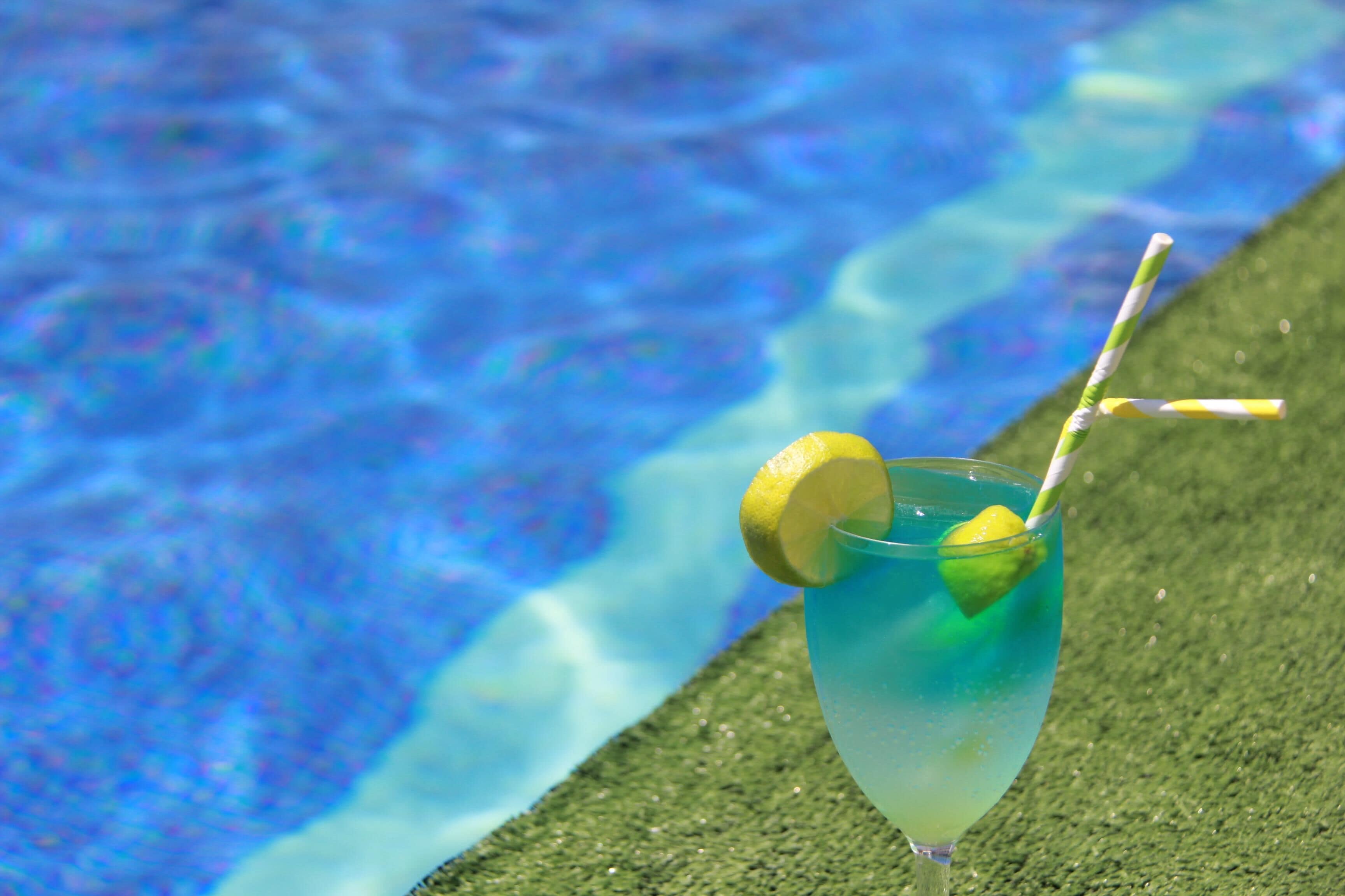 Un vaso de cóctel con pajita y una rodaja de limón junto a una piscina.