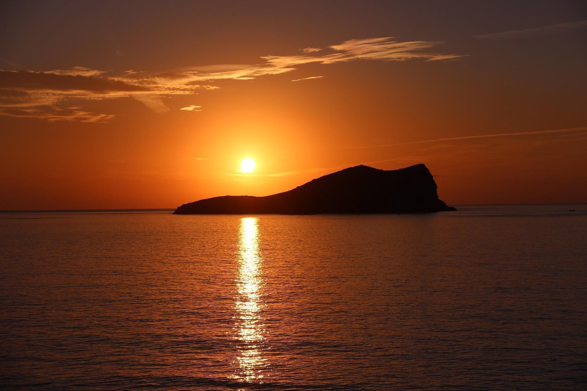 Een zonsondergang boven een rustige zee, met de silhouet van een berg of heuvel.