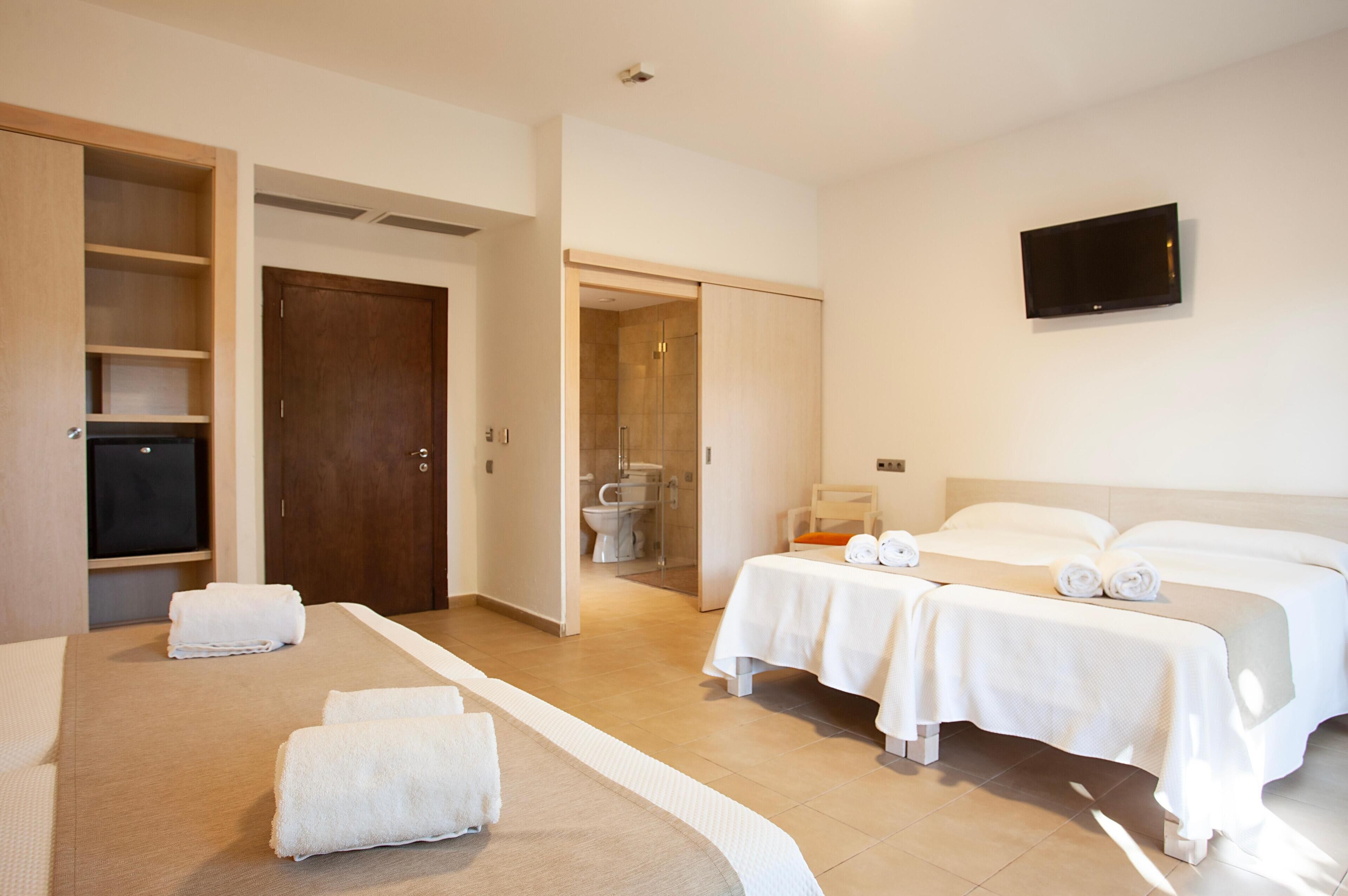 Une chambre d’hôtel avec un lit, deux tables de chevet, une télévision et une salle de bain visible à travers une porte ouverte.