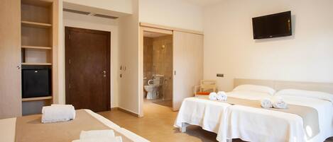 Une chambre d’hôtel avec un lit, deux tables de chevet, une télévision et une salle de bain visible à travers une porte ouverte.