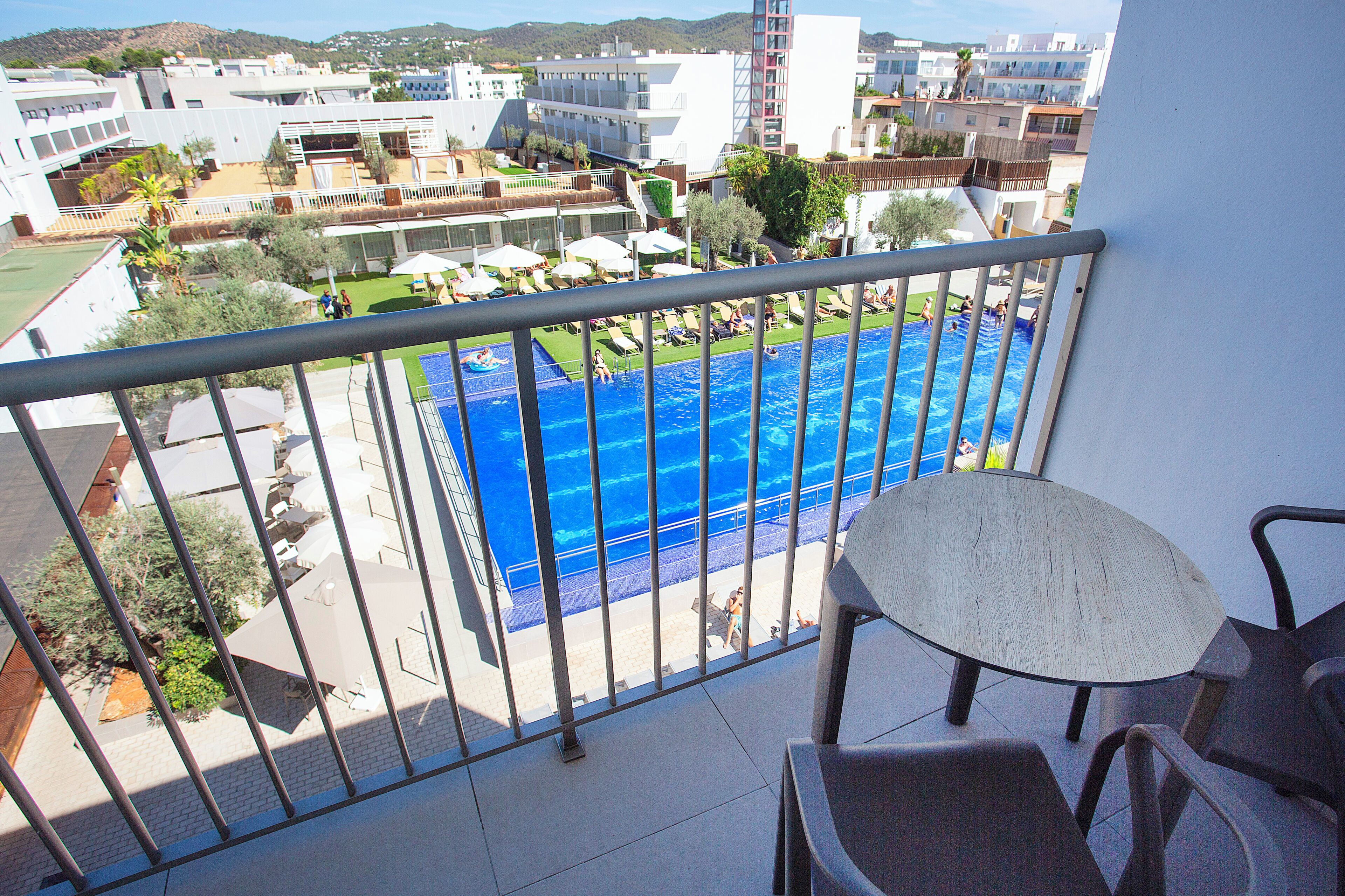 Un balcón con vista a una piscina, mobiliario exterior y edificios circundantes.