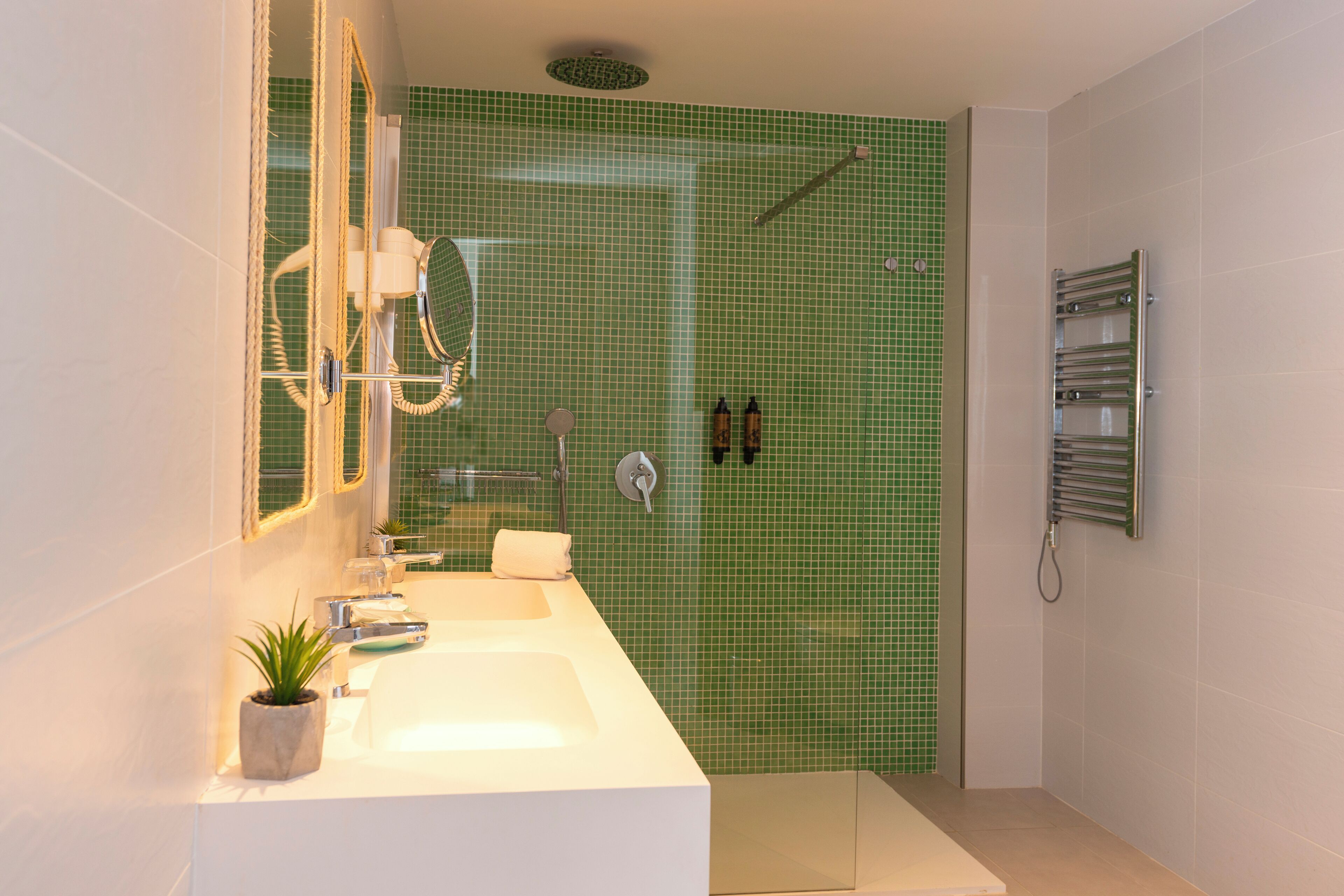 Un baño con un lavamanos blanco, un espejo, una ducha con pared de azulejos verdes y un perchero para toallas.