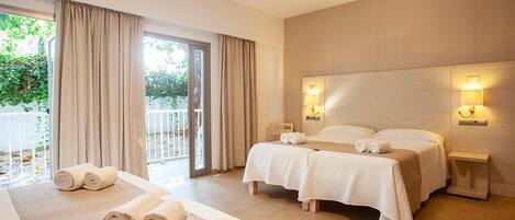 Habitación de hotel con dos camas, balcón y vistas a zonas verdes.