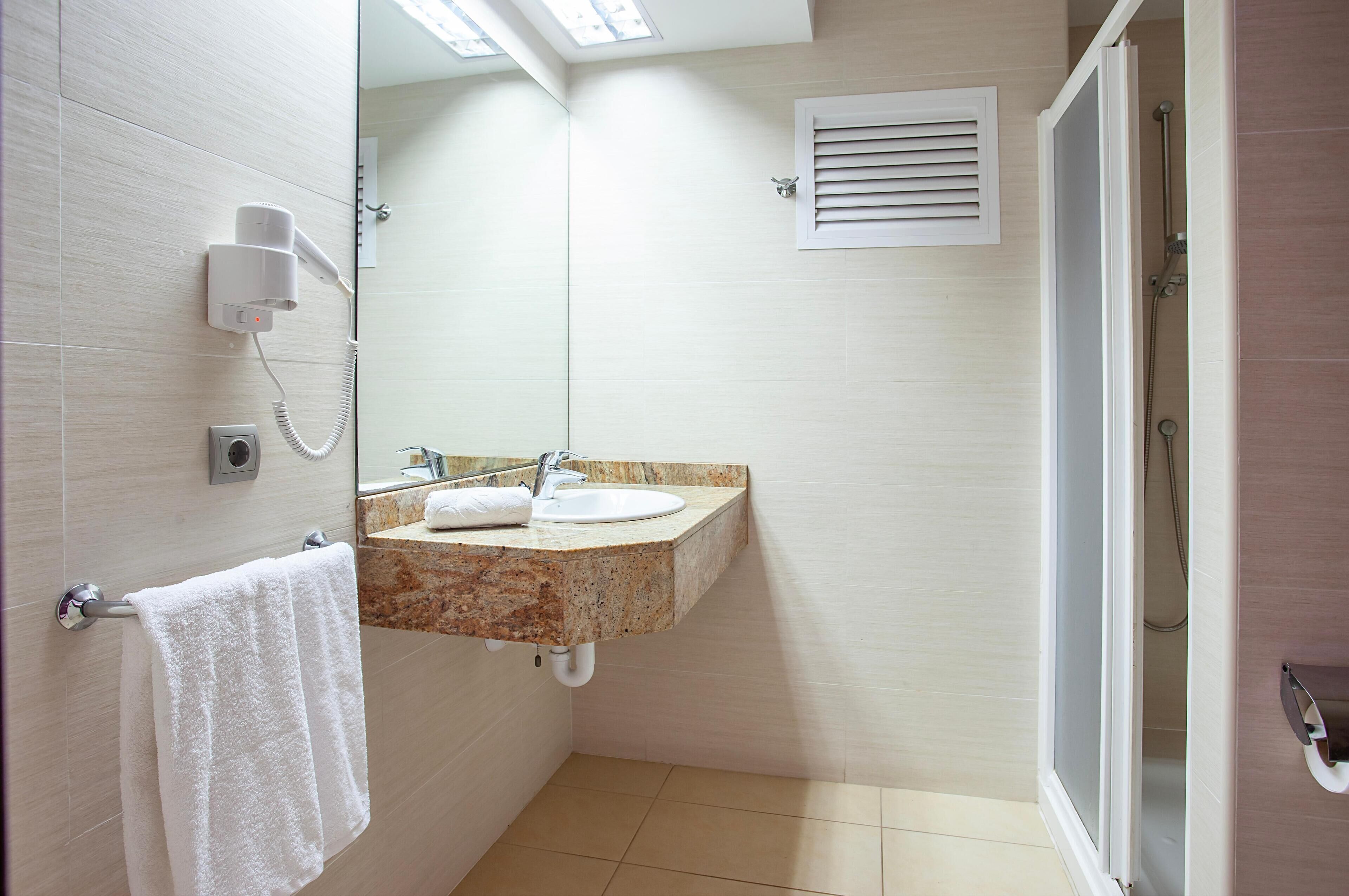 A bathroom with a sink, mirror, towel rack, and a shower area.