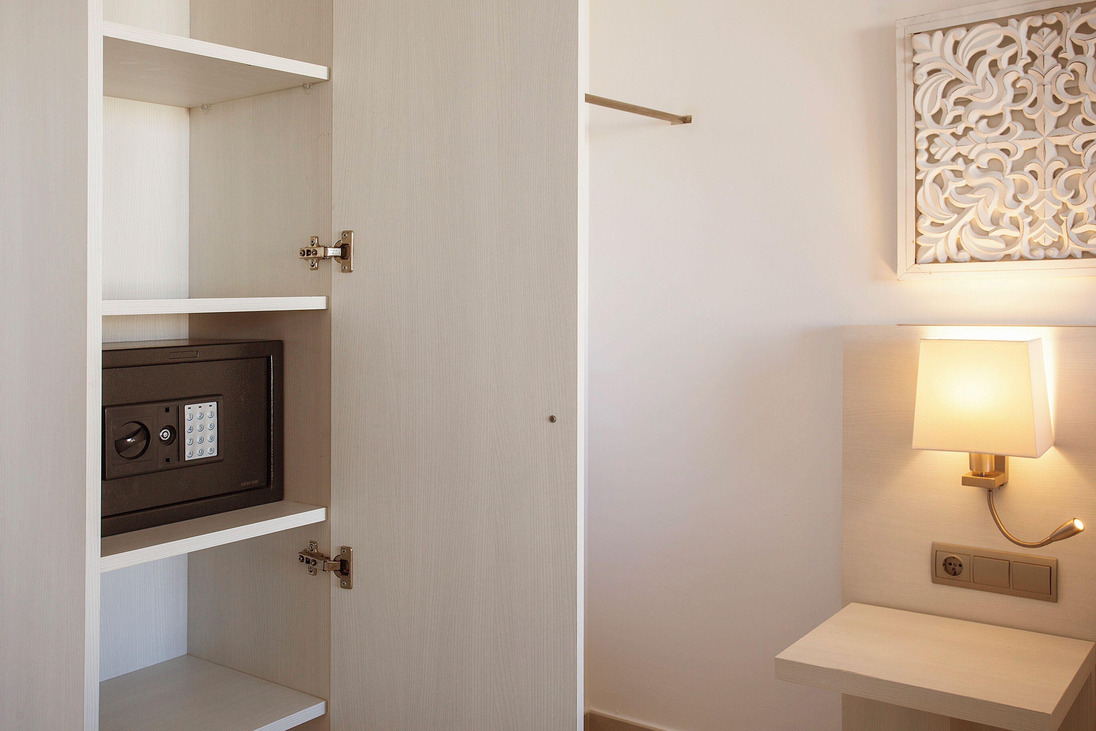 Ein Zimmer mit einem fest eingebauten Safe, einem Nachttisch und einer Wandleuchte.