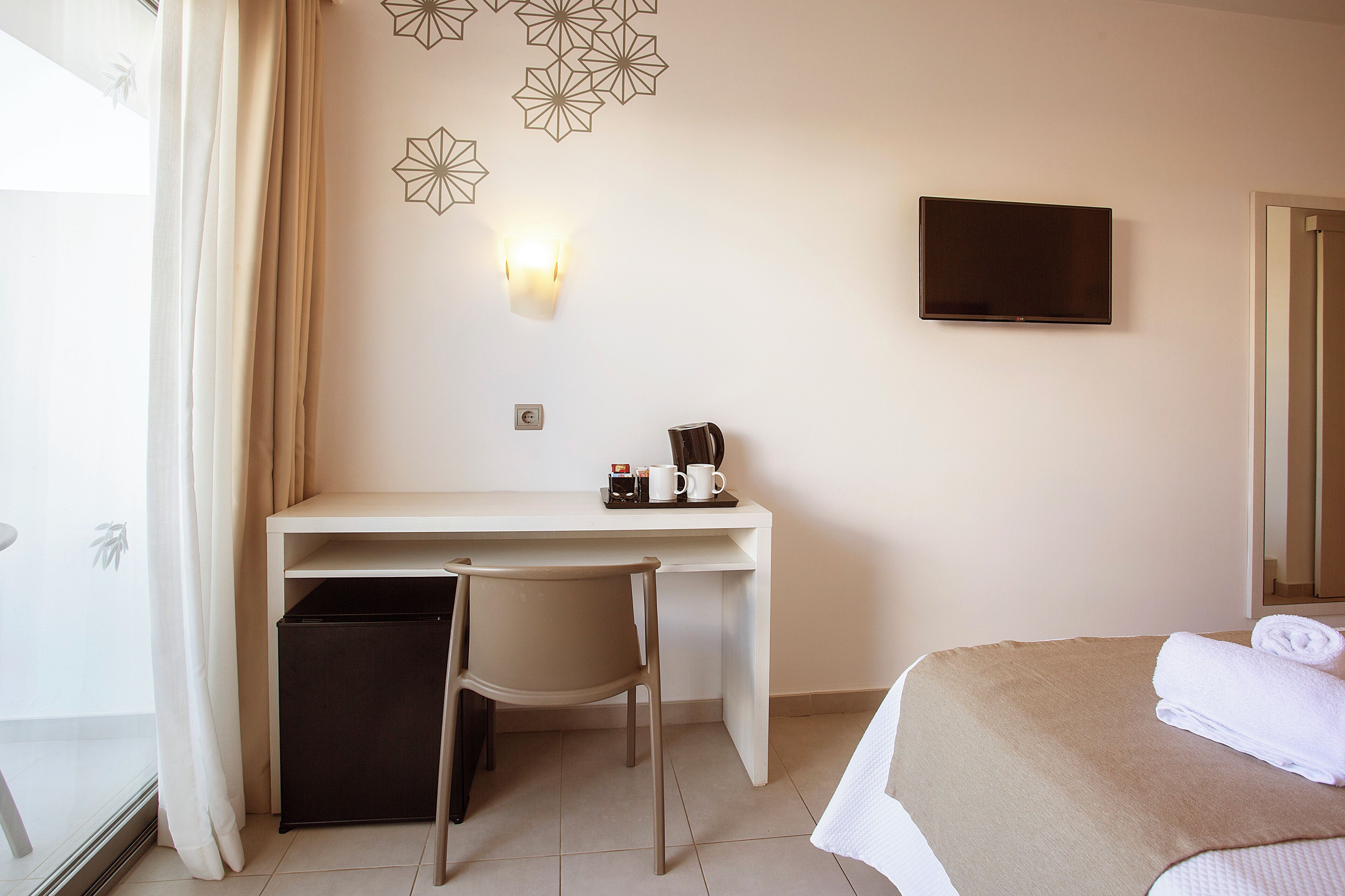 Habitación de hotel con escritorio, silla, cama, televisor y luz adosada a la pared.