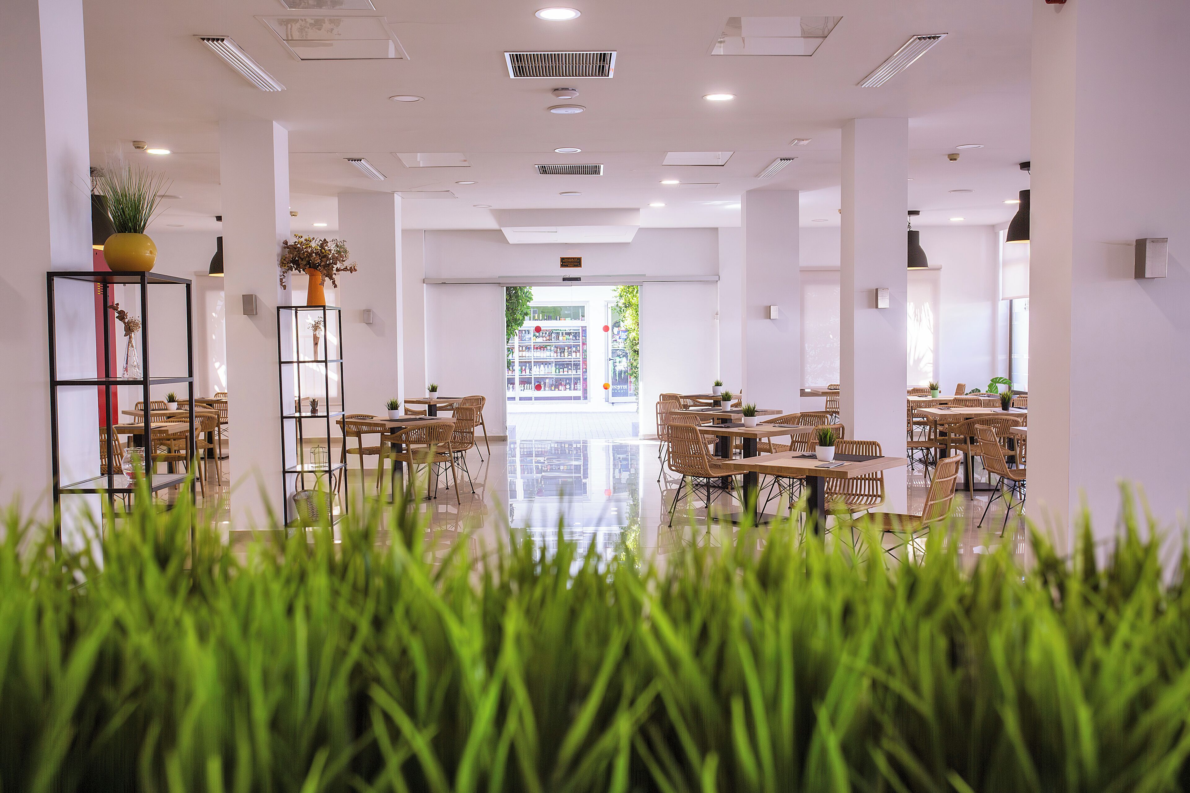 Un interior moderno con un espacio central abierto, rodeado de mesas y sillas, y vistas al exterior a través de un gran ventanal.