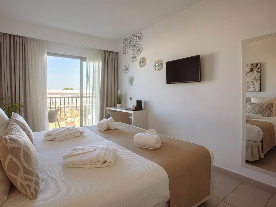 Ein Hotelzimmer mit einem großen Bett, einem Schreibtisch, einem Sessel und einem Balkon mit Vorhängen.