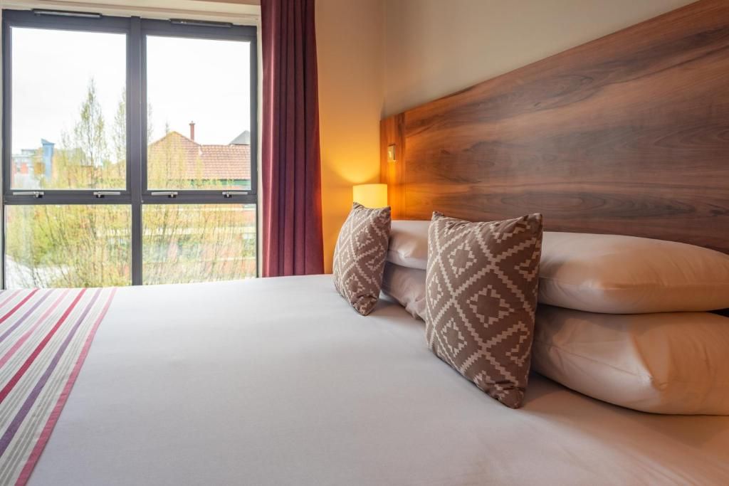 A hotel room with a large bed, a wooden headboard, and a view of the outside.