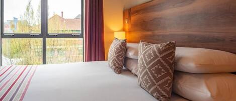 A hotel room with a large bed, a wooden headboard, and a view of the outside.