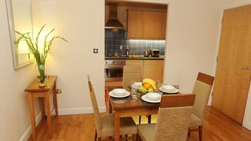A dining area with a wooden table, chairs, and a vase of green plants.