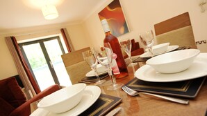 A dining table set with white plates, wine glasses, and a bottle of wine, with a red chair and a painting on the wall. - PREMIER SUITES Bristol Redcliffe (Bristol)
