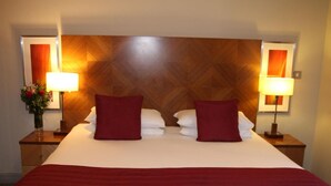 A hotel room with a large bed, two red pillows, white linens, and two bedside lamps. - PREMIER SUITES Bristol Redcliffe (Bristol)