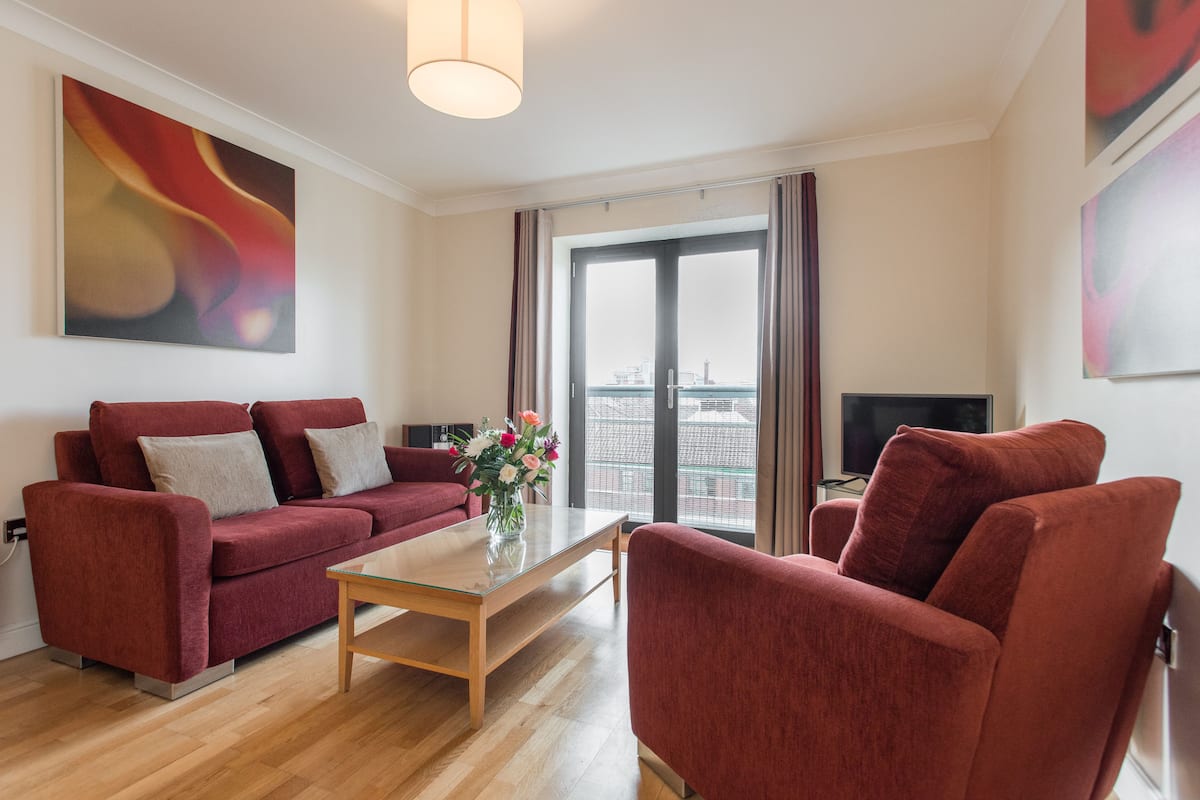 Una sala de estar moderna con un sofá rojo, una mesa de centro de vidrio y un televisor.