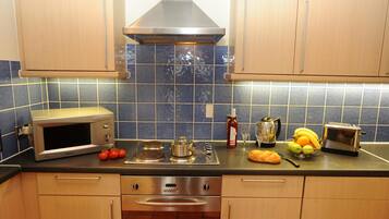 Een keuken met een magnetron, broodrooster en een verscheidenheid aan fruit en groenten op het aanrecht.