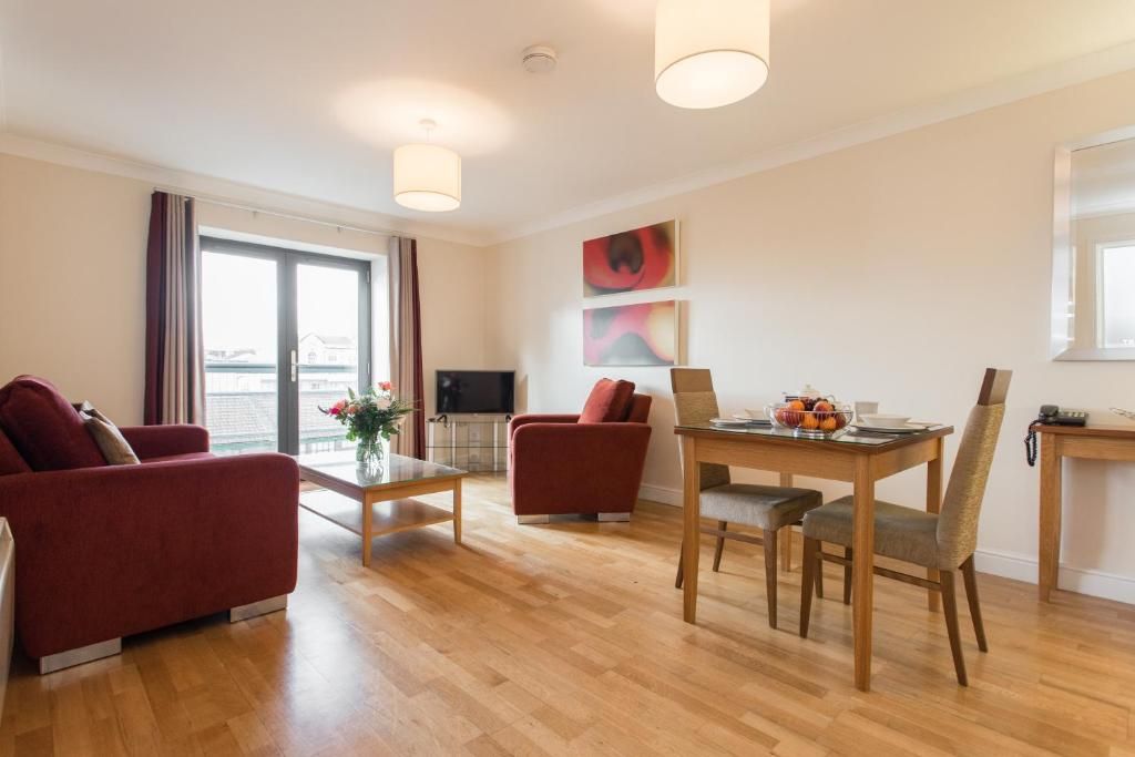 Een moderne woonkamer met een rode bank, een eettafel met stoelen, een flatscreen televisie en kunst aan de muur.