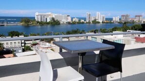 A balcony with a table and chair overlooking a cityscape and a body of water. - Hotel Miramar (San Juan)