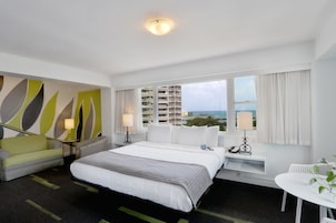 Habitación de hotel con cama, escritorio, silla y vista al océano, además de un diseño moderno en la pared.