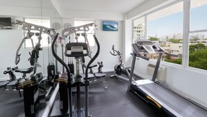 A gym with various exercise equipment, large windows, and a view of buildings. - Hotel Miramar (San Juan)
