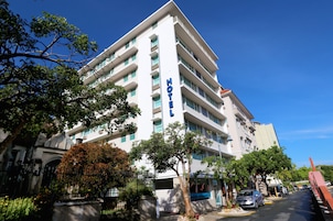 Un hotel de varios pisos con un llamativo letrero que dice 'HOTEL' en la fachada, rodeado de árboles y coches estacionados.