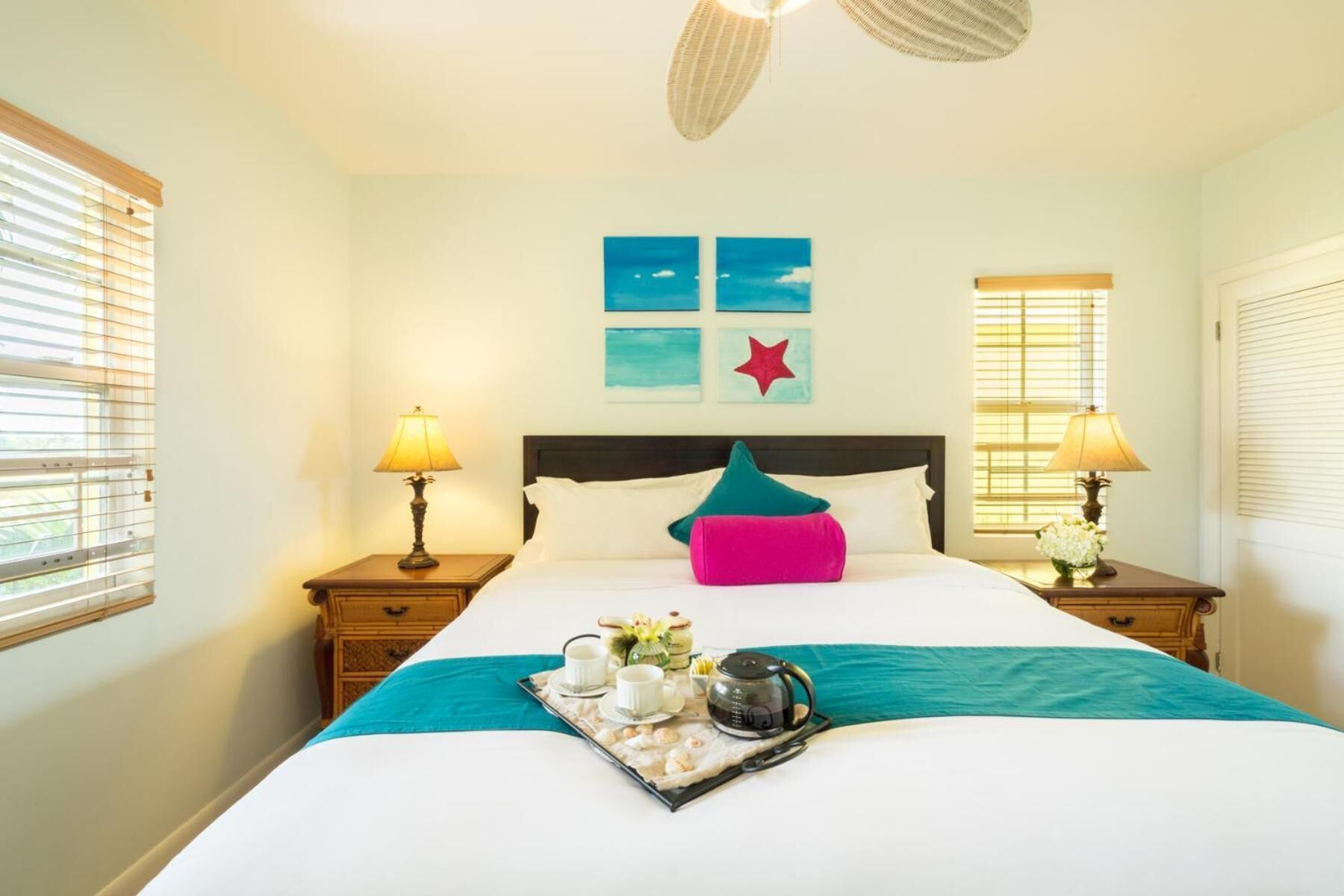 Een hotelkamer met een bed, twee nachtkastjes, een raam met zonwering en een plafondventilator.