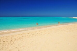 Perto da praia, areia branca, espreguiçadeiras, guarda-sóis 