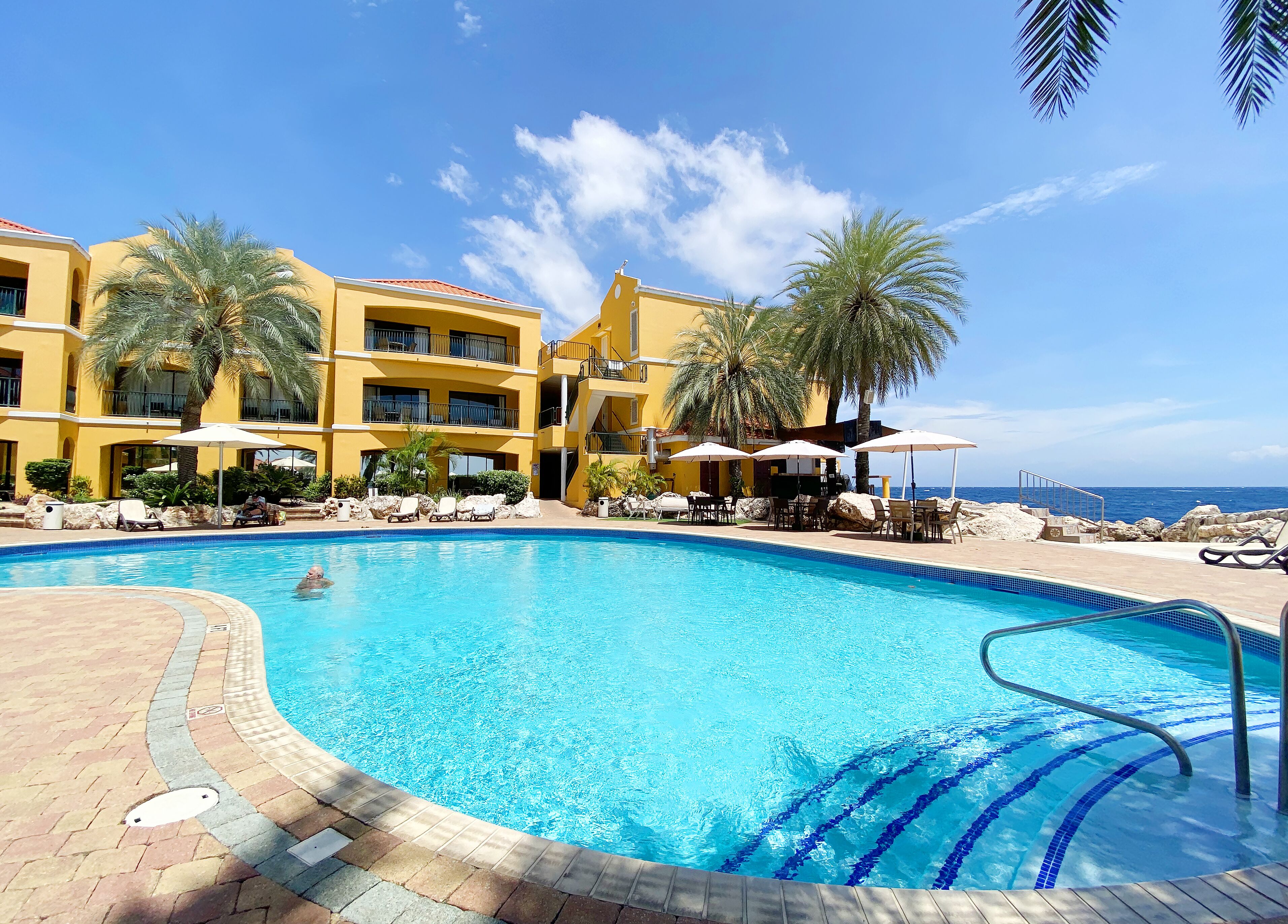Un hotel con piscina, palmeras y vista al océano.