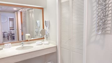 A bathroom with a large mirror, two sinks, a towel rack, and a trash bin.