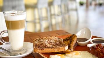Une table en bois dressée pour le petit-déjeuner, avec des toasts, des œufs, du bacon et du café.