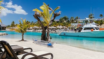 Una playa con sillas de descanso, un bote y palmeras.