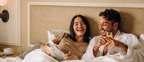 A couple in a hotel room, reading a book and drinking juice.