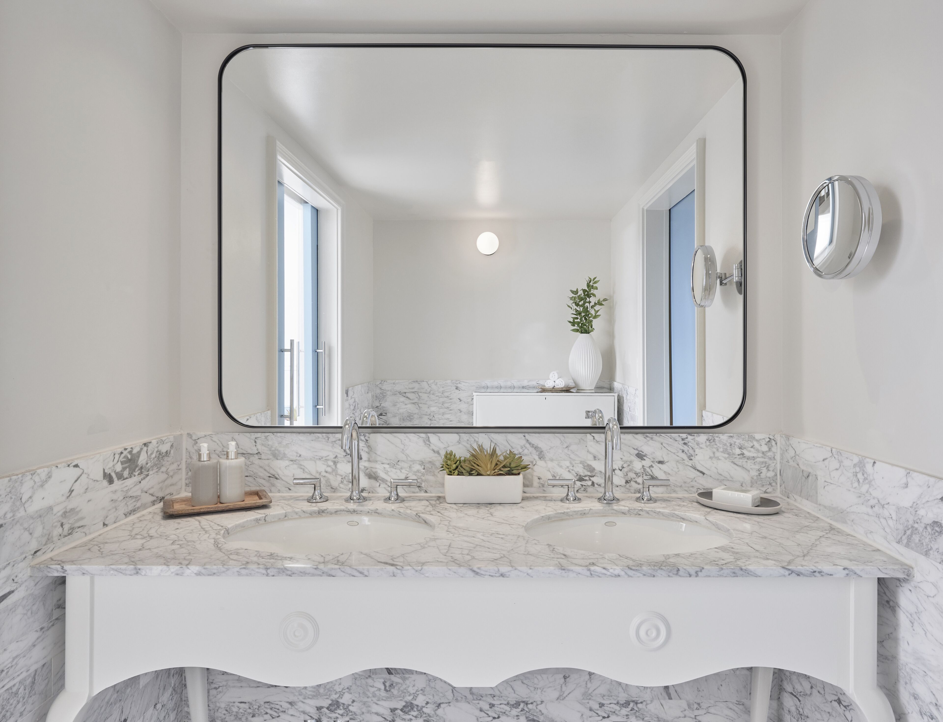 A bathroom with a large mirror, two sinks, and a white vanity.