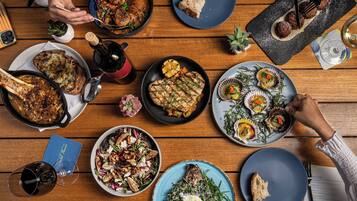 A wooden table with various dishes, including grilled meat, salads, and bread.