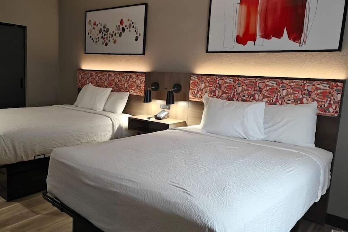 Habitación de hotel con dos camas, una mesita de noche con lámpara y obras de arte en las paredes.