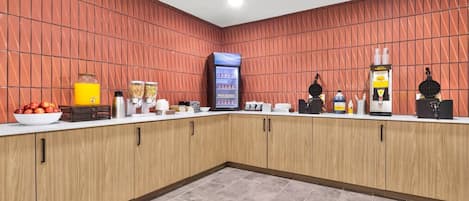 A modern kitchen with a red tiled backsplash, a refrigerator, a coffee machine, and various food dispensers.