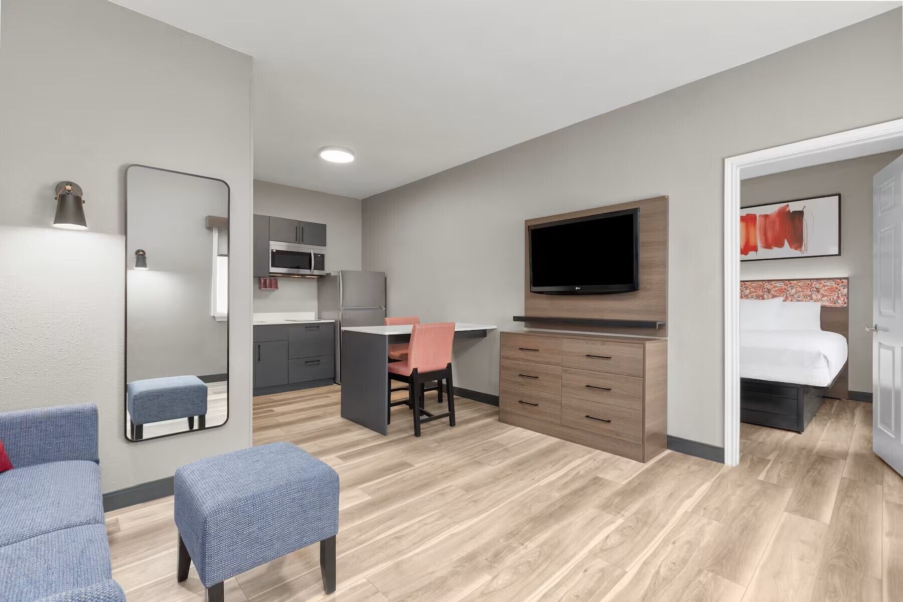Habitación de hotel con cama, televisión, escritorio con silla, kitchenette y zona de estar con dos sillas.