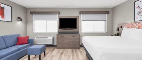 A hotel room with a bed, a sofa, a TV, and an air conditioning unit.