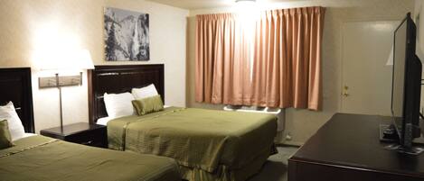 Habitación de hotel con dos camas, un escritorio, un televisor y una ventana con cortinas.