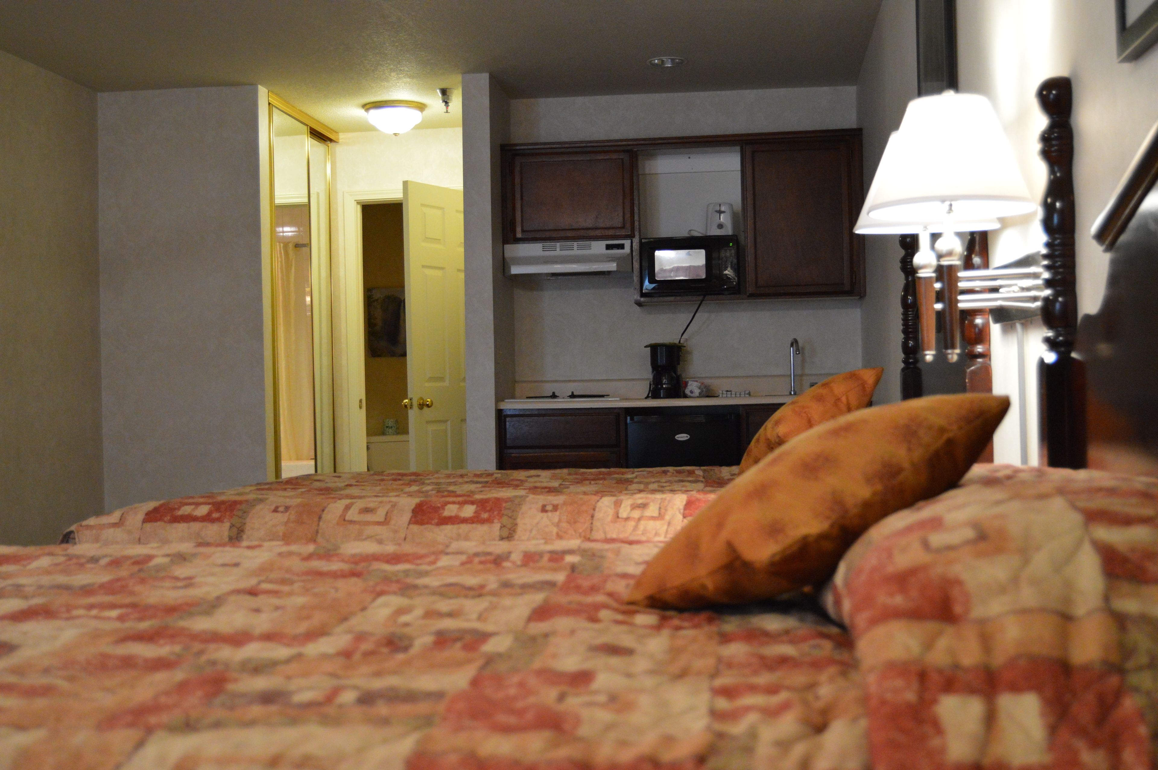 A hotel room with a bed, a bedside lamp, a microwave, and a kitchenette.
