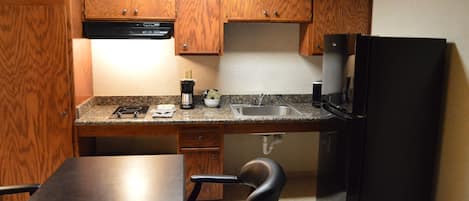 Una cocina compacta con armarios de madera, un refrigerador negro, una cafetera y un lavamanos.