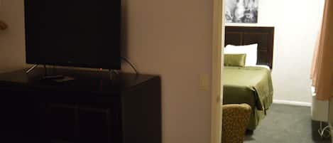 A hotel room with a television on a cabinet, a bed with green bedding, and a chair.