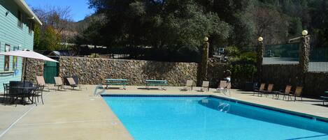 A swimming pool with lounge chairs and tables, surrounded by a stone wall and trees.