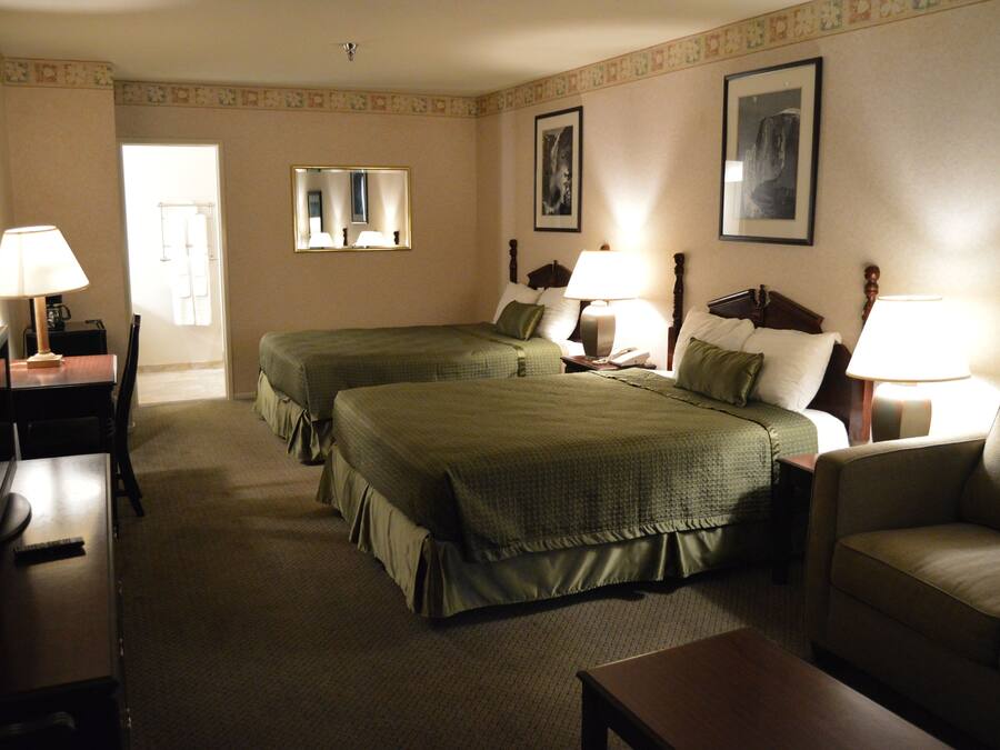 A hotel room with two beds, a desk, a chair, and a sofa. There are lamps on both sides of the beds.