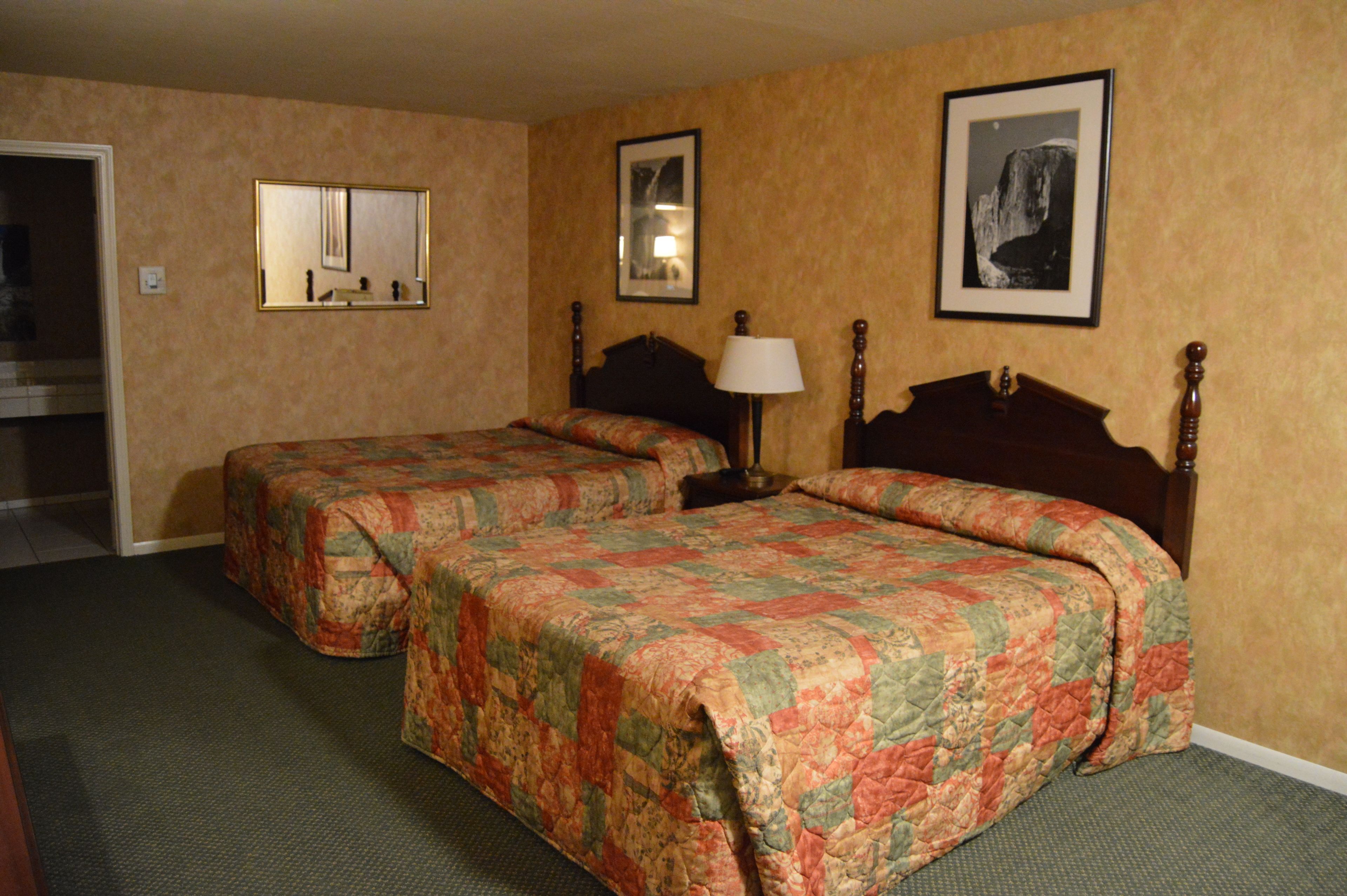 A hotel room with two single beds, a mirror, a nightstand with a lamp, and framed pictures on the wall.