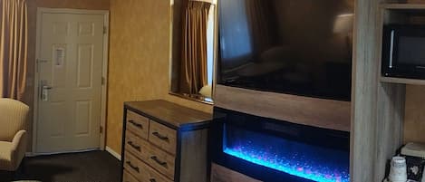 Una habitación de hotel con cama, dos sillas, un escritorio con lámpara, televisión, microondas y un acuario.
