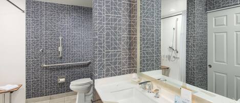 Een moderne badkamer met een betegelde achterwand in geometrische patronen, een wit wastafelmeubel met spiegel, en een douchehoek.
